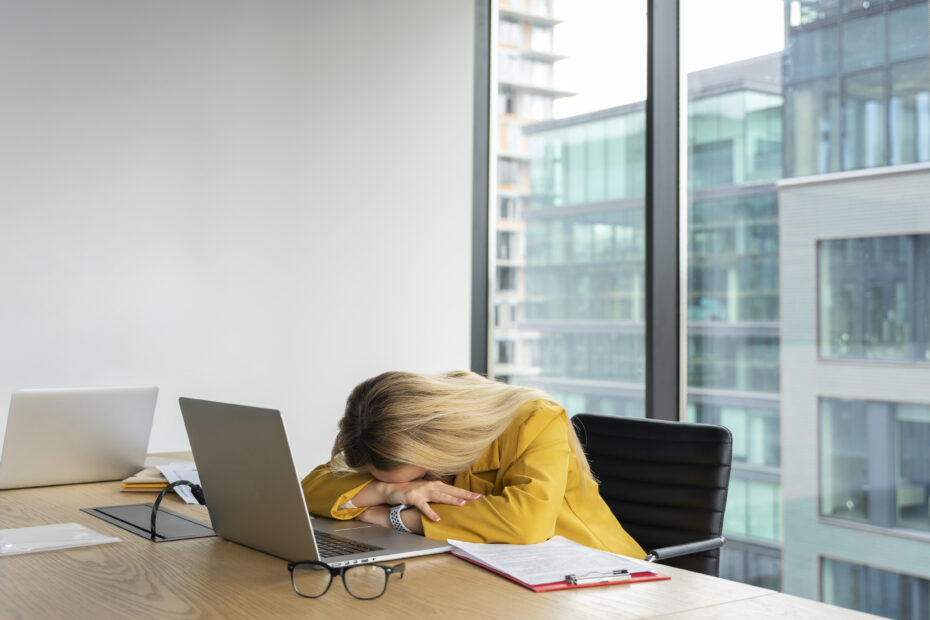 Mujer en la oficina con mucha presión y ansiedad sin ser productiva con la cabeza entre las manos.